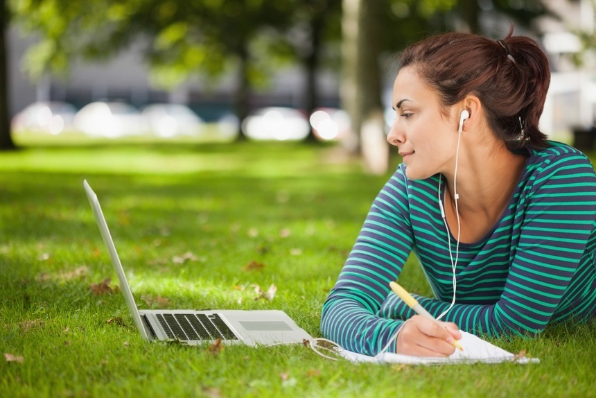 Attractive casual student lying on grass taking notes on campus at college