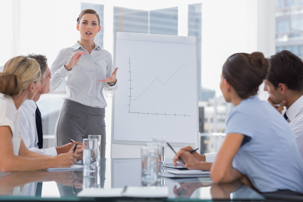 Businesswoman giving explication in front of a growing chart on a whiteboard during a meeting