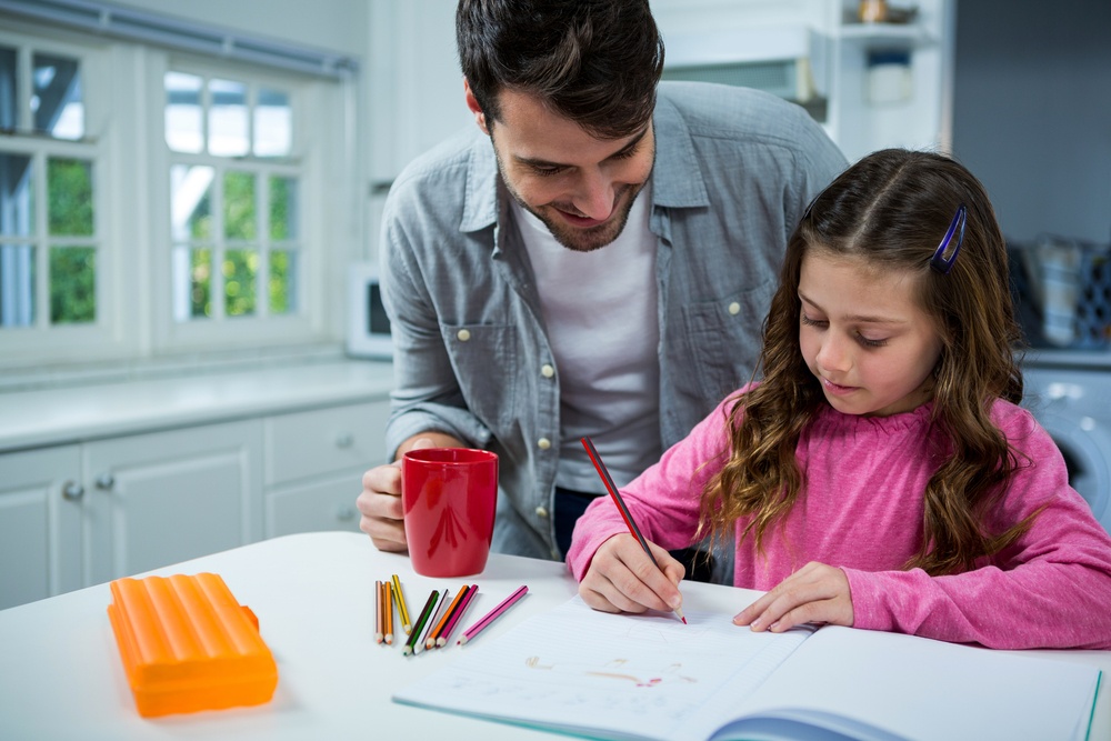 Father helping girl with homework at home in the kitchen