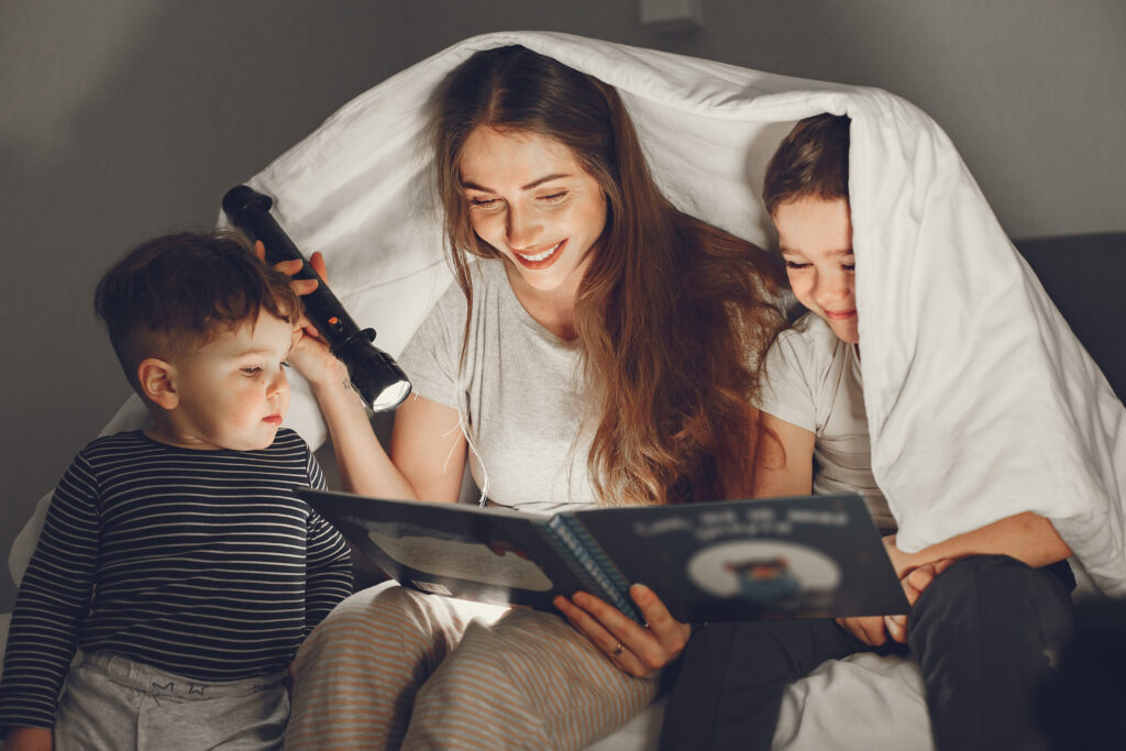 family under the blanket in bed reading book scaled